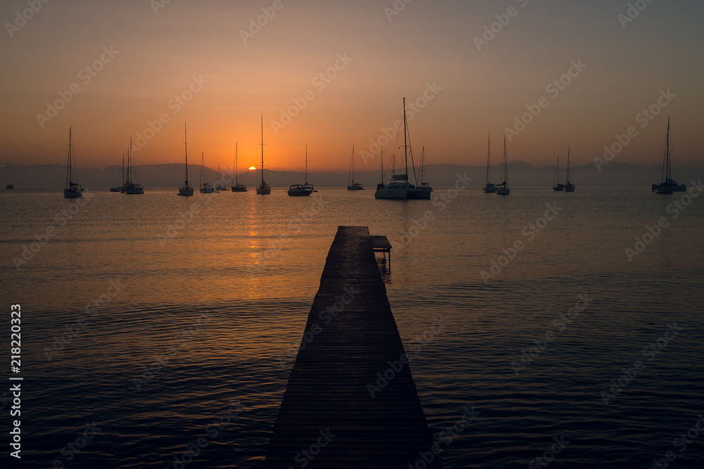 Scenic view of wooden pier and yachts at the calm sea on beautiful pink and orange sunset. Mountains on background. Dusk