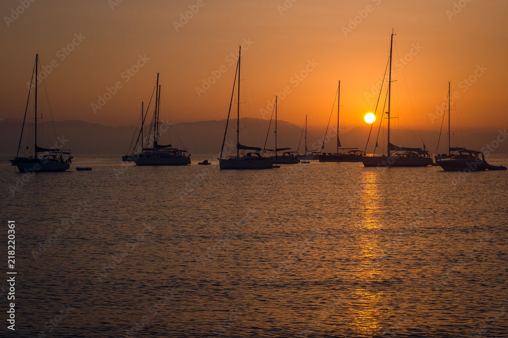 Breathtaking view of sailing boats and yachts in marina bay on beautiful orange sunset over the mountains. Greece