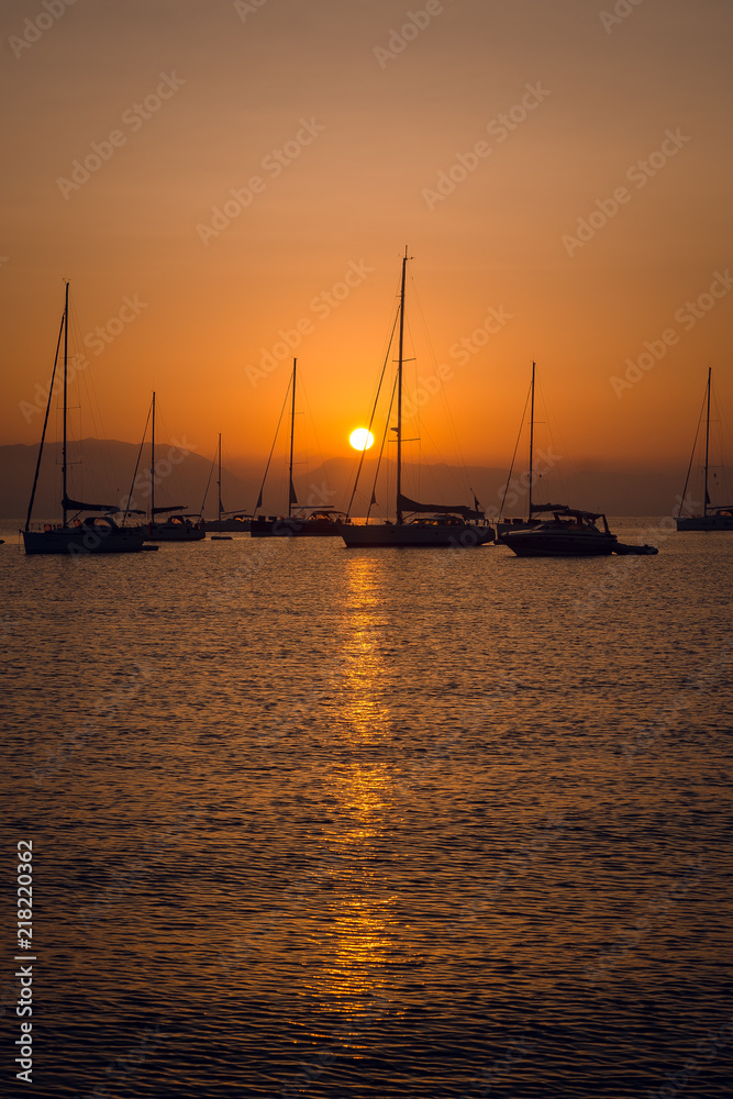 Scenic view of sailing boats and yachts in marina bay on beautiful orange sunset over the mountains. Greece