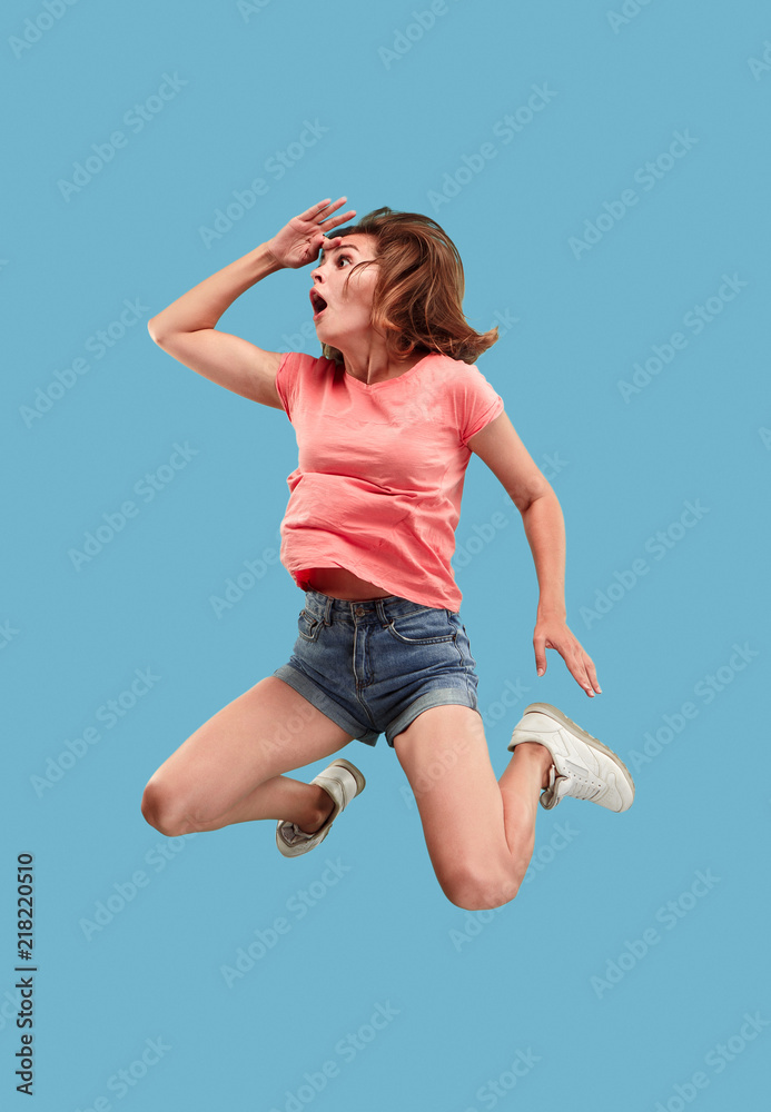 Freedom in moving. Mid-air shot of pretty happy surprised young woman jumping against blue studio background. Runnin girl in motion or movement. Human emotions and facial expressions concept Freedom in moving. Mid-air shot of pretty happy surprised young woman jumping against blue studio background. Runnin girl in motion or movement. Human emotions and facial expressions concept