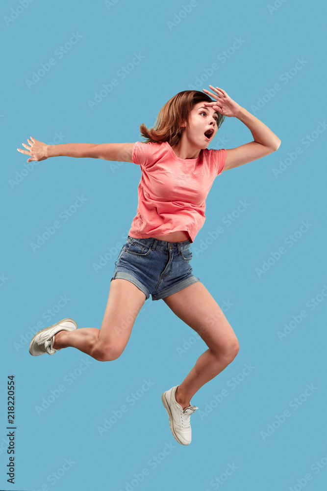 Freedom in moving. Mid-air shot of pretty happy surprised young woman jumping against blue studio background. Runnin girl in motion or movement. Human emotions and facial expressions concept Freedom in moving. Mid-air shot of pretty happy surprised young woman jumping against blue studio background. Runnin girl in motion or movement. Human emotions and facial expressions concept