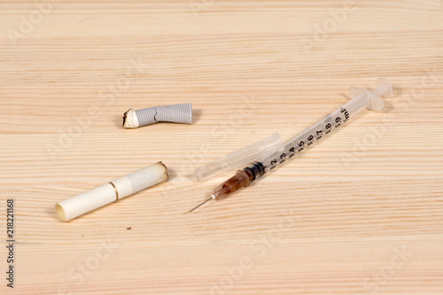 Syringe and several cigarette butts on a wooden countertop