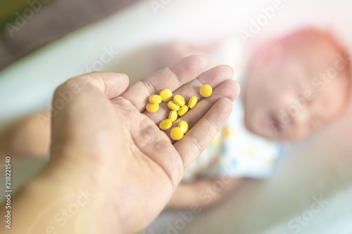 Selective focus Medicine pills or capsules in hand, palm or fingers with blur crying baby or newborn background. Drug prescription for treatment medication, person taking vitamin, antibiotic.