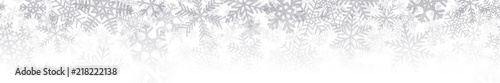 Christmas horizontal seamless banner or background of many layers of snowflakes of different shapes, sizes and transparency. Gradient from gray to white