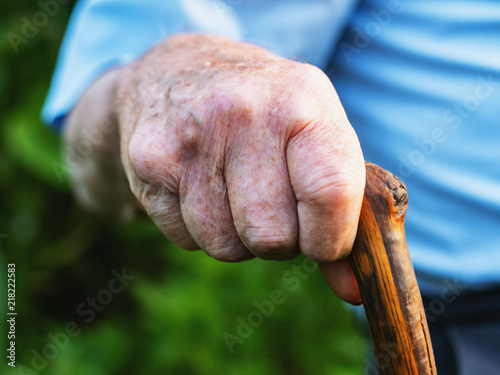 wrinkled old man' hands crossed on the stick. Close-up of a pensive grandfather sitting alone outdoors and rests on a cane. © kohanova1991