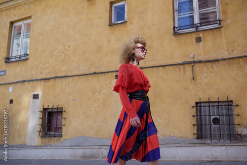 Young woman with curly hair in red retro dress. Walk around the city © Iulia