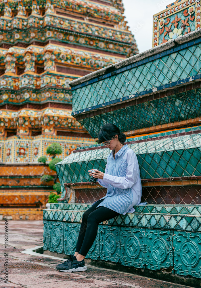 Fototapeta premium Asian woman traveler sit and check photo in camera near ancient pagoda buildings background- Wat pho temple- Bangkok-Thailand- Asia.