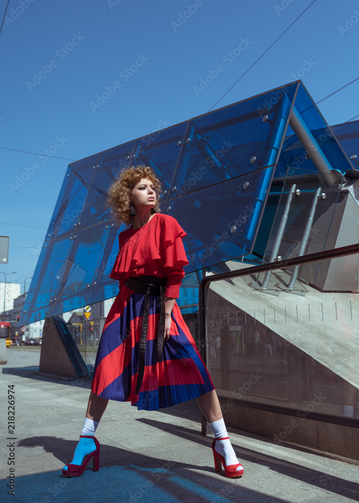 Young woman with curly hair in red retro dress. Young woman walking in the street. Fashion concept