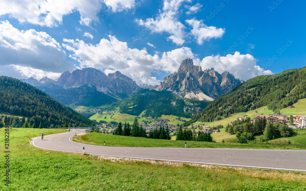 Panoramic view of Corvara in Badia village in the summer season (in the foreground there is a road with two cyclists) Panoramic view of Corvara in Badia village in the summer season (in the foreground there is a road with two cyclists)