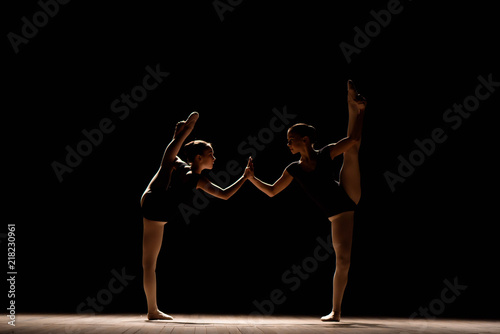 Flexible ballerinas stretch on a dark lighted scene