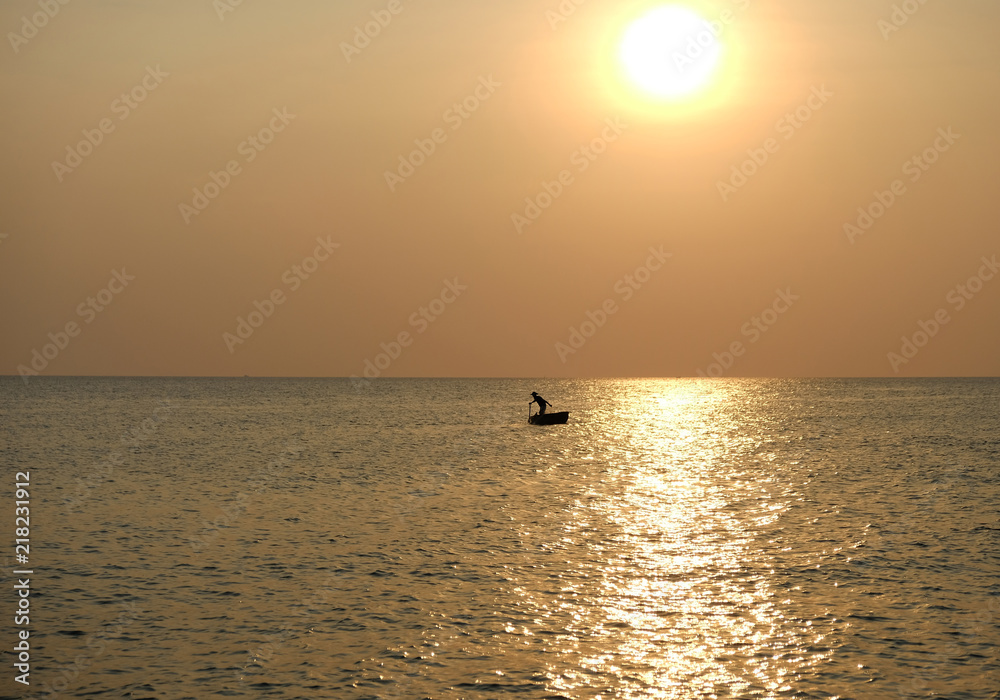 Silhouette of fisherman in boat in sea during sunset next to bright sun-glade on water. Phu Quoc, Vietnam