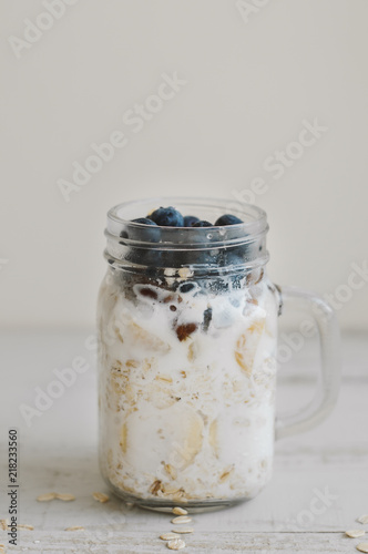 Homemade overnight oats with fruits, coconut milk, whole grain and blueberries in a tall jar on wooden table