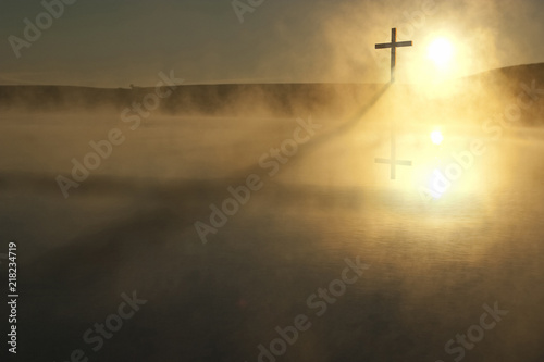Fotografie, Obraz This Sunrise Cross on a misty lake casts a lengthy shadow and reflection on this