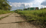 Polna droga, trawiasta łąka z prawej, za nią kolorowy budynek spalarni śmieci w Krakowie, Polska, małe chmurki na niebie