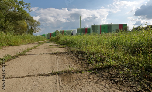 Polna droga, trawiasta łąka z prawej, za nią kolorowy budynek spalarni śmieci w Krakowie, Polska, małe chmurki na niebie