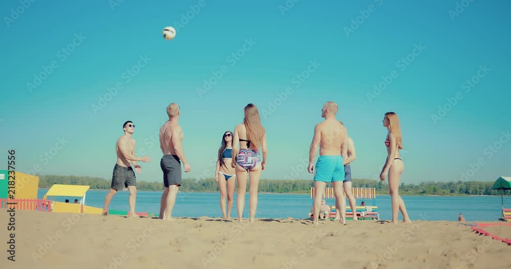 Group of young girls and guys playing beach volleyball. Slow motion