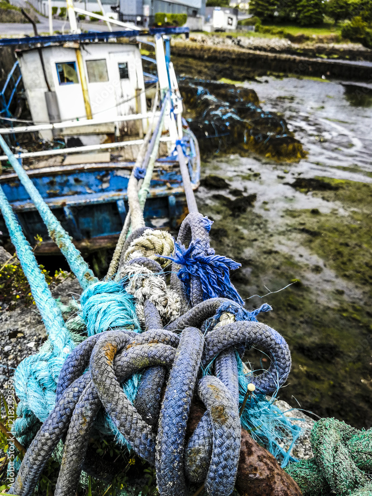 Old blue and white fishing boat, moored up in Kilkieran Quay in Connemara, Ireland. Showing the bow of the boat and the knotted ropes.