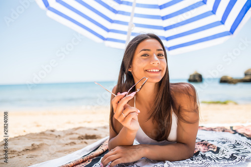 Young woman in sunglasses resting under a umbrella on a beach near the sea