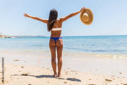 Woman on Beach standing with arms outstretched against turquoise sea. Rear view of female wearing bikini with raised hands. Carefree tourist is enjoying vacation at beach.