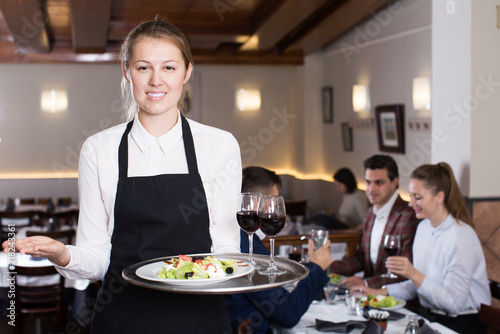 Smiling waitress with serving tray meeting restaurant guests