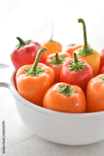white bowl full of orange red yellow baby sweet peppers 