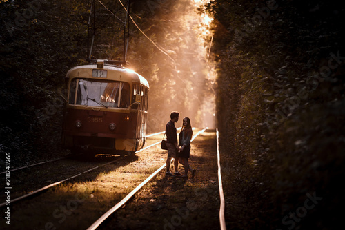 Young couple  standing on the tram rails  in high trees alley in stunning evening sunlight.