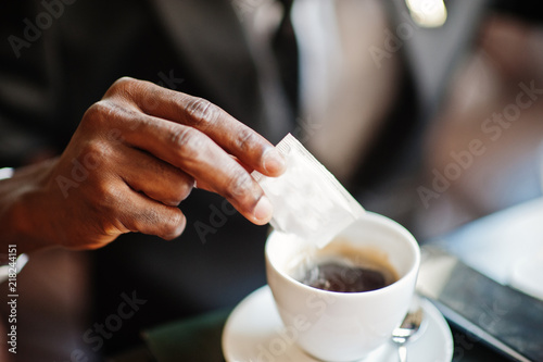 Close up hand of african american business man pours sugar into coffee.