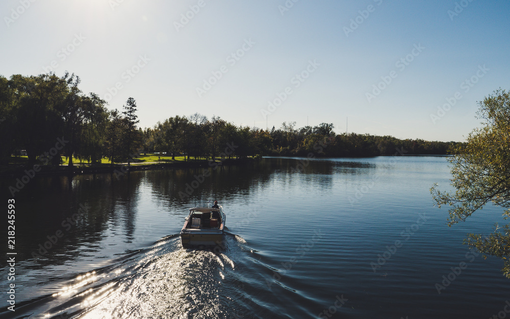 Obraz premium boat from behind driving on a beautiful river in a park during sunny summer day on toronto island