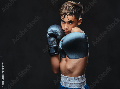 Portrait of a handsome shirtless young boxer wearing gloves. Isolated on a dark background. © Fxquadro