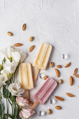 Homemade frozen ice cream popsicles from fruits and berries on table whith flowers and ingridients, top view