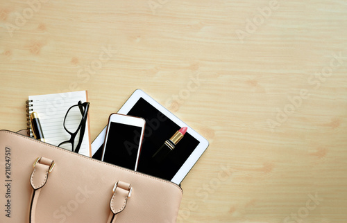Business woman's luxury everyday-life travel accessories flat lay on light wooden background with formal beige handbag, cellphone, blank notepad, luxury pen, glasses and lipstick with big copy space 