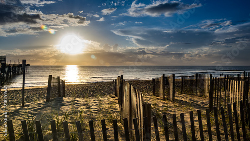 Fototapeta Naklejka Na Ścianę i Meble -  Erosion fencing and plants help protect the dunes from the constant ocean breeze and storm surge. Sunrise over a calm Atlantic Ocean in the Outer Banks of North Carolina.