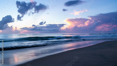 A beautiful pastel morning sky. The colorful sunrise light is reflected on the wet sand at the beach. Tranquil and serene coastal paradise.