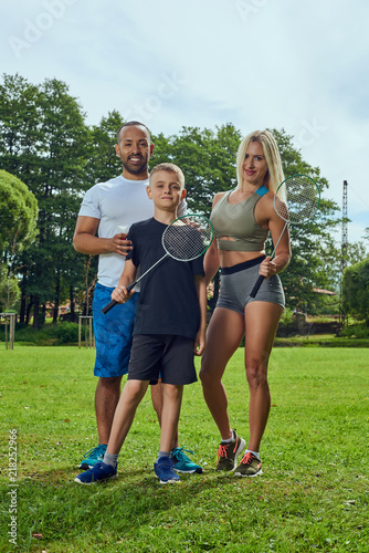 Fototapeta Naklejka Na Ścianę i Meble -  Sports multinational family; mother, father and his son doing sport exercises together outdoor