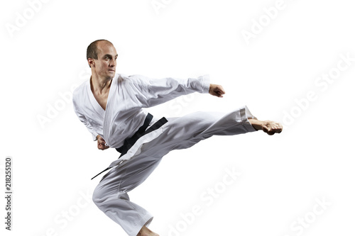 A man with a black belt trains a kick in a jump isolated