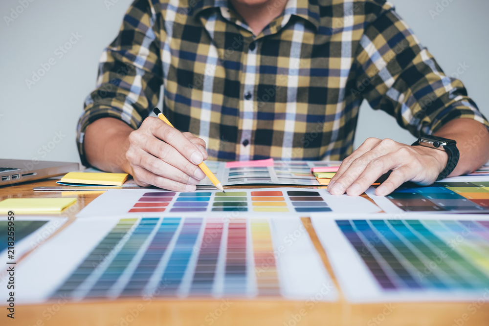 Creative graphic designer using graphics tablet to choosing color swatch samples chart for selection coloring with work tools and accessories while working with computer at studio Creative graphic designer using graphics tablet to choosing color swatch samples chart for selection coloring with work tools and accessories while working with computer at studio