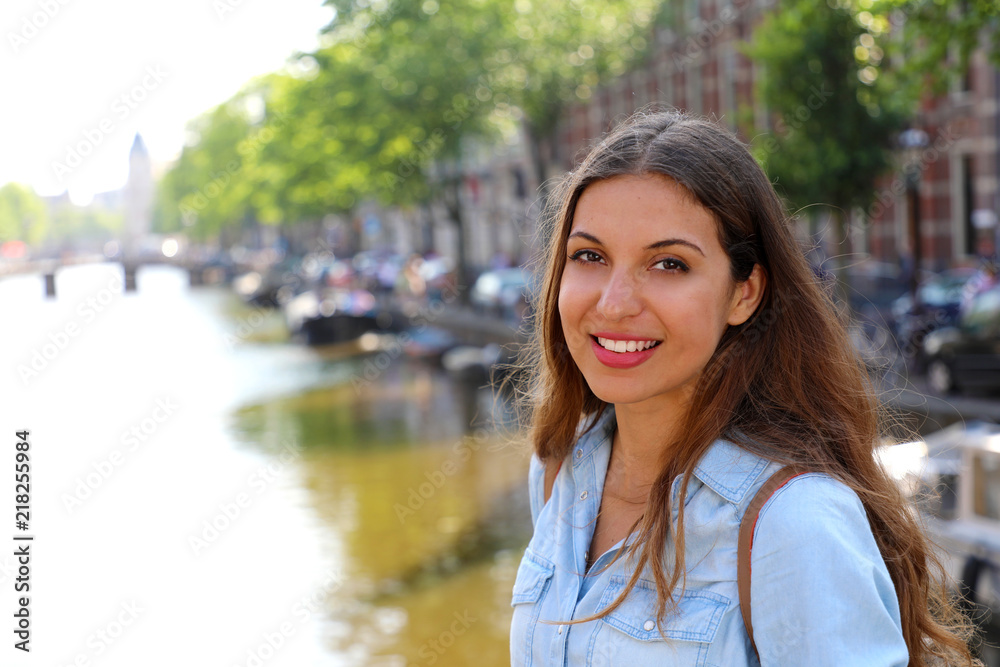 Fototapeta premium Smiling urban girl on bridge looking at camera. Young beautiful woman wearing casual jeans shirt in Amsterdam, Netherlands.