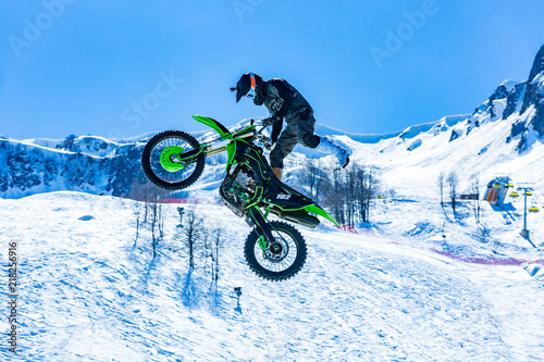 racer on a motorcycle in flight  jumps and takes off on a springboard against the snowy mountains