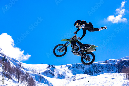 racer on a motorcycle in flight, jumps and takes off on a springboard against the snowy mountains © Georgii