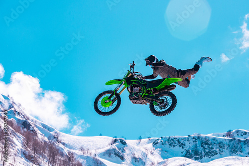 racer on a motorcycle in flight, jumps and takes off on a springboard against the snowy mountains