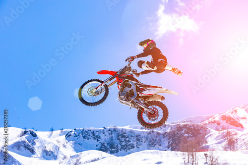 Fototapeta Naklejka Na Ścianę i Meble -  racer on a motorcycle in flight, jumps and takes off on a springboard against the snowy mountains