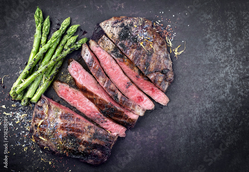 Barbecue dry aged wagyu flank steak sliced with green asparagus as top view on an old rusty board with copy space right photo