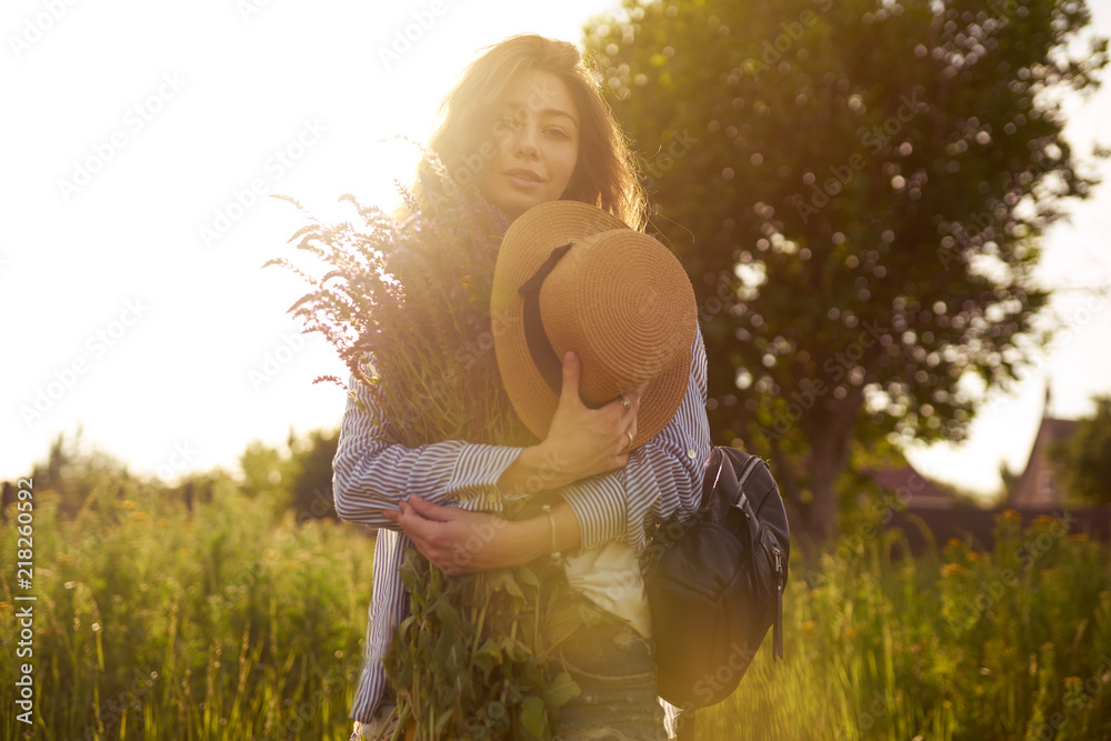 Fototapeta premium A beautiful girl with a bouquet of lavender. She is dressed in a blue shirt, a white T-shirt. A good summer sunny evening. The girl is smiling. Sunny sunset light