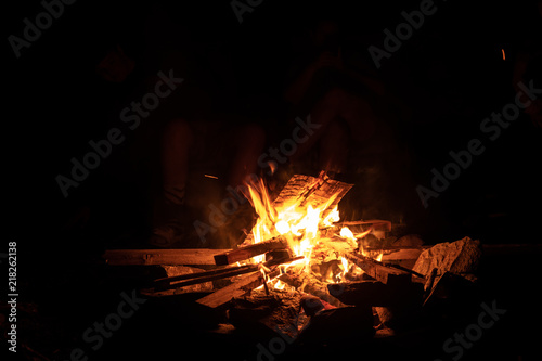 A wood fire blazes in a fire pit as family members and friends gather around at night to roast marshmallows