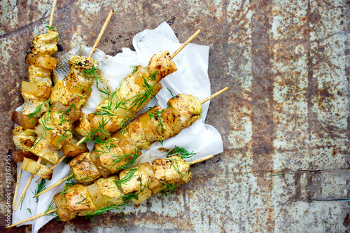 Chicken skewers with pineapple slices with dill and lemon on white paper napkin on an old metal background top view