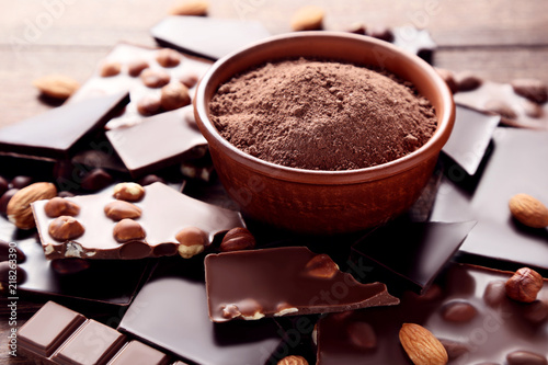 Chocolate pieces with cocoa powder in bowl on wooden table