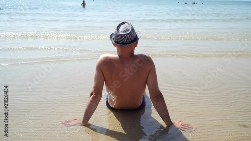 Summer lifestyle HD video of pretty young suntanned man in a hat. Enjoying life and sitting on the beach, time to travel. Looking at the sea photo