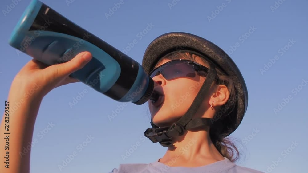A child in a helmet is drinking water. A girl in a bicycle helmet is drinking water. A child in a helmet is drinking water. A girl in a bicycle helmet is drinking water.