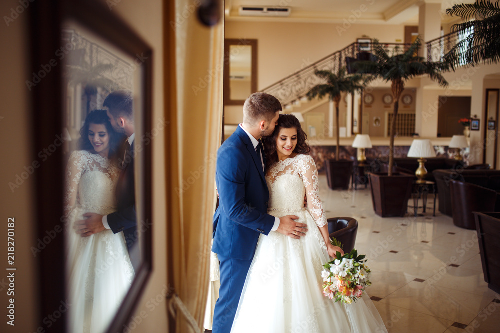 Naklejka premium Beautiful Bride and Groom enjoy each other in the nice hall of the hotel. happy romantic young couple celebrating their marriage.Sexy kissing stylish couple of lovers close up portrait. wedding
