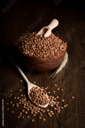 Lentil in a wooden bowl on a wooden background near the ears of wheat. wooden spoon with Lentil